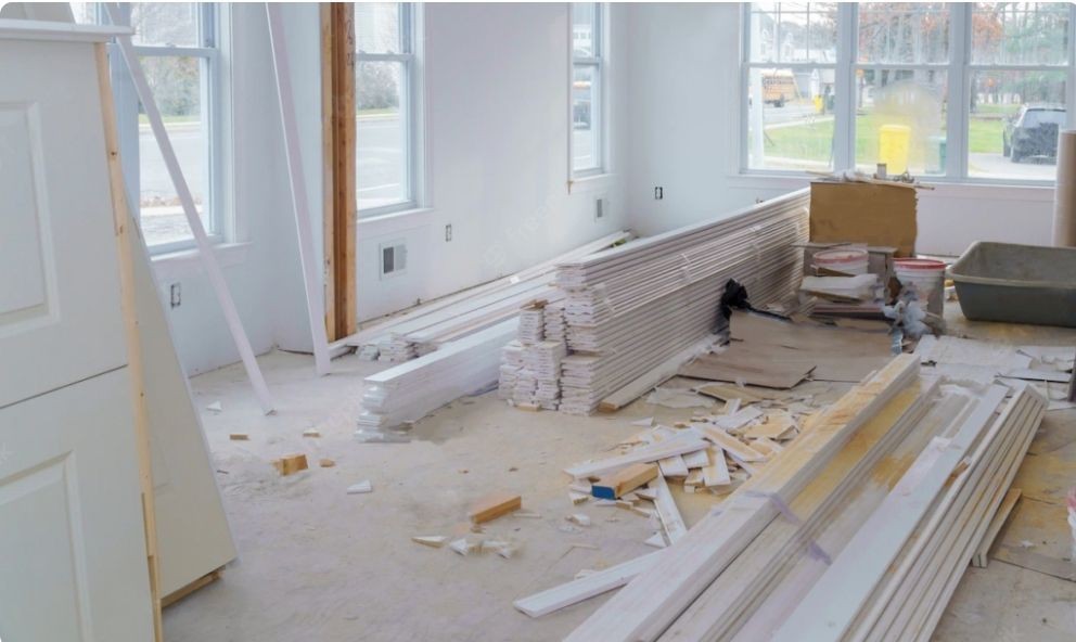 Interior of a room under construction with stacked wood planks and scattered tools on the floor.
